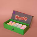 Box of colorful bath bombs with a 'Treats' label on a pink background